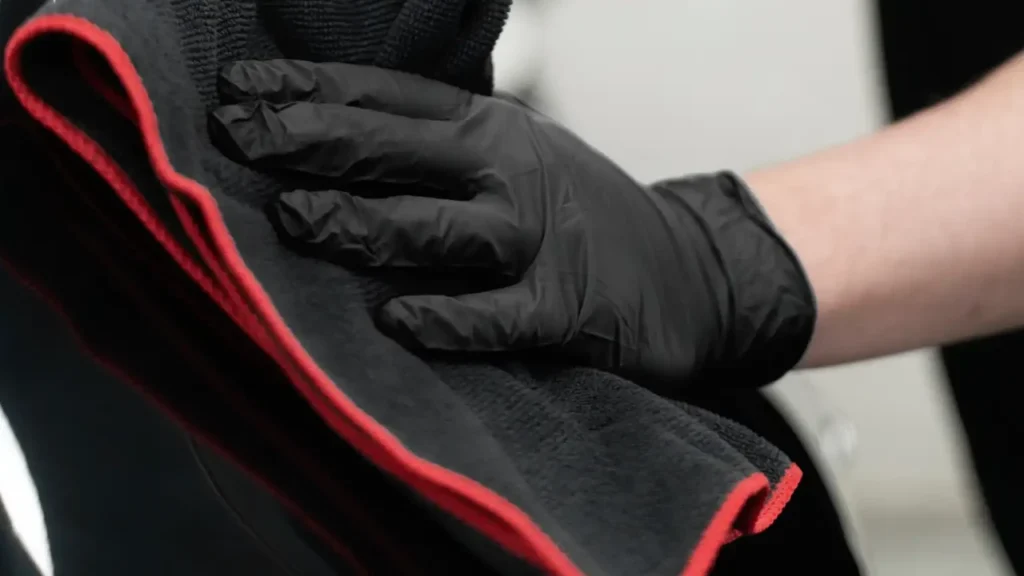 Hand i svart handske lägger en mikrofiberhandduk mot bilens lack vid torkning